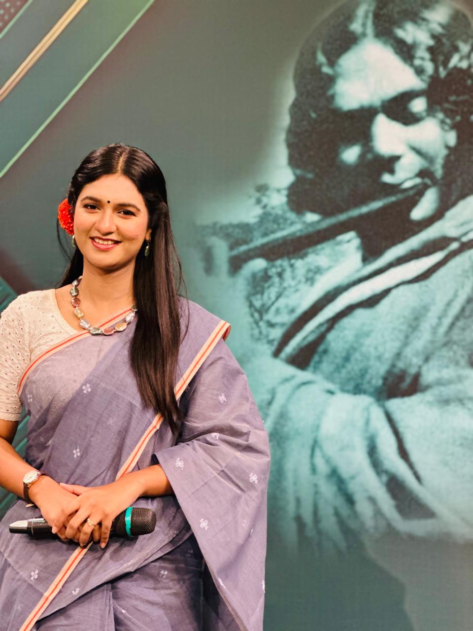 Sanjida Rahman in a grey saree standing before a Kazi Nazrul Islam tribute backdrop