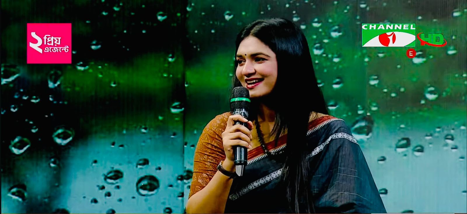 Close-up of Sanjida Rahman speaking into a microphone during a Channel i broadcast