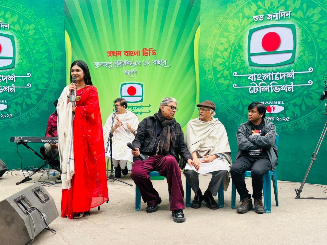 Sanjida Rahman in a red saree hosting on stage with seated guests behind her