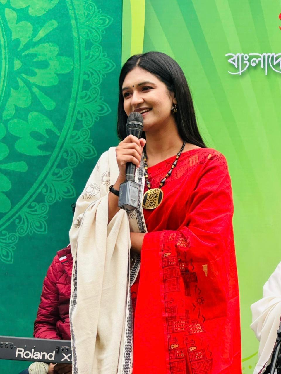 Close-up of Sanjida Rahman in a red saree speaking into a microphone at an outdoor event